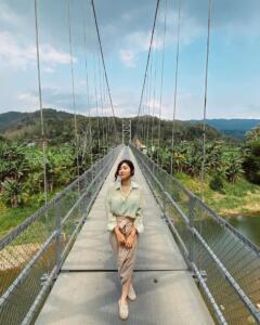 Berfoto di tengah jembatan dengan latar belakang pepohonan dan bukit yang memukau